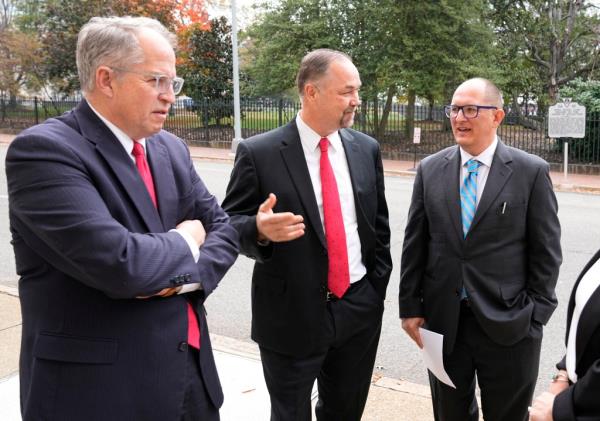Three men in suits speaking on a sidewalk.